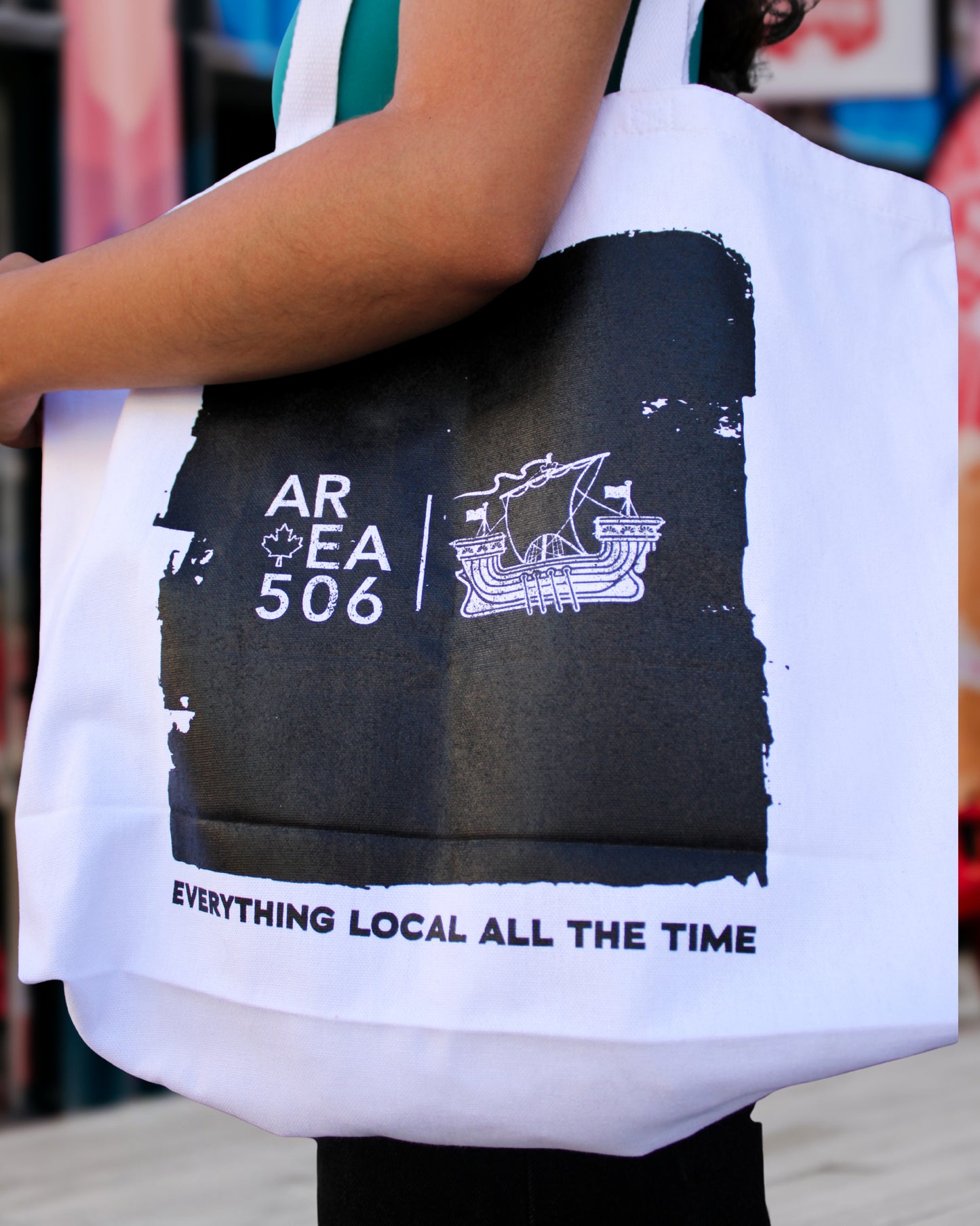 Tote bag with black and white design featuring text and a logo, held by a person.