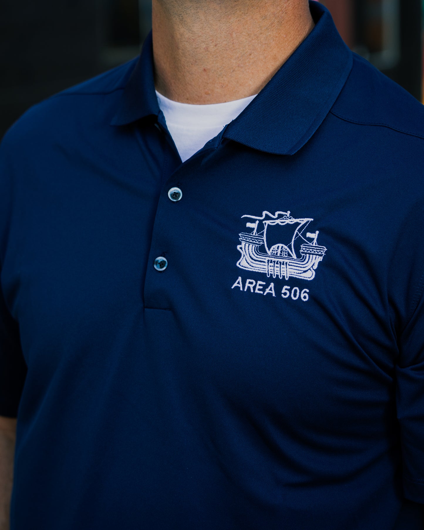 Navy blue polo shirt with 'AREA 506' logo on a person wearing it.