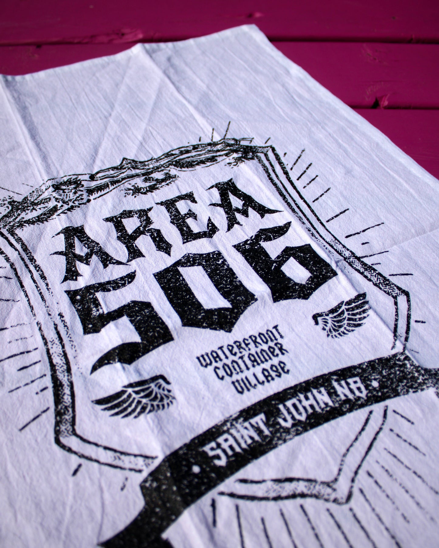White kitchen towel with black text and graphics on a pink background.