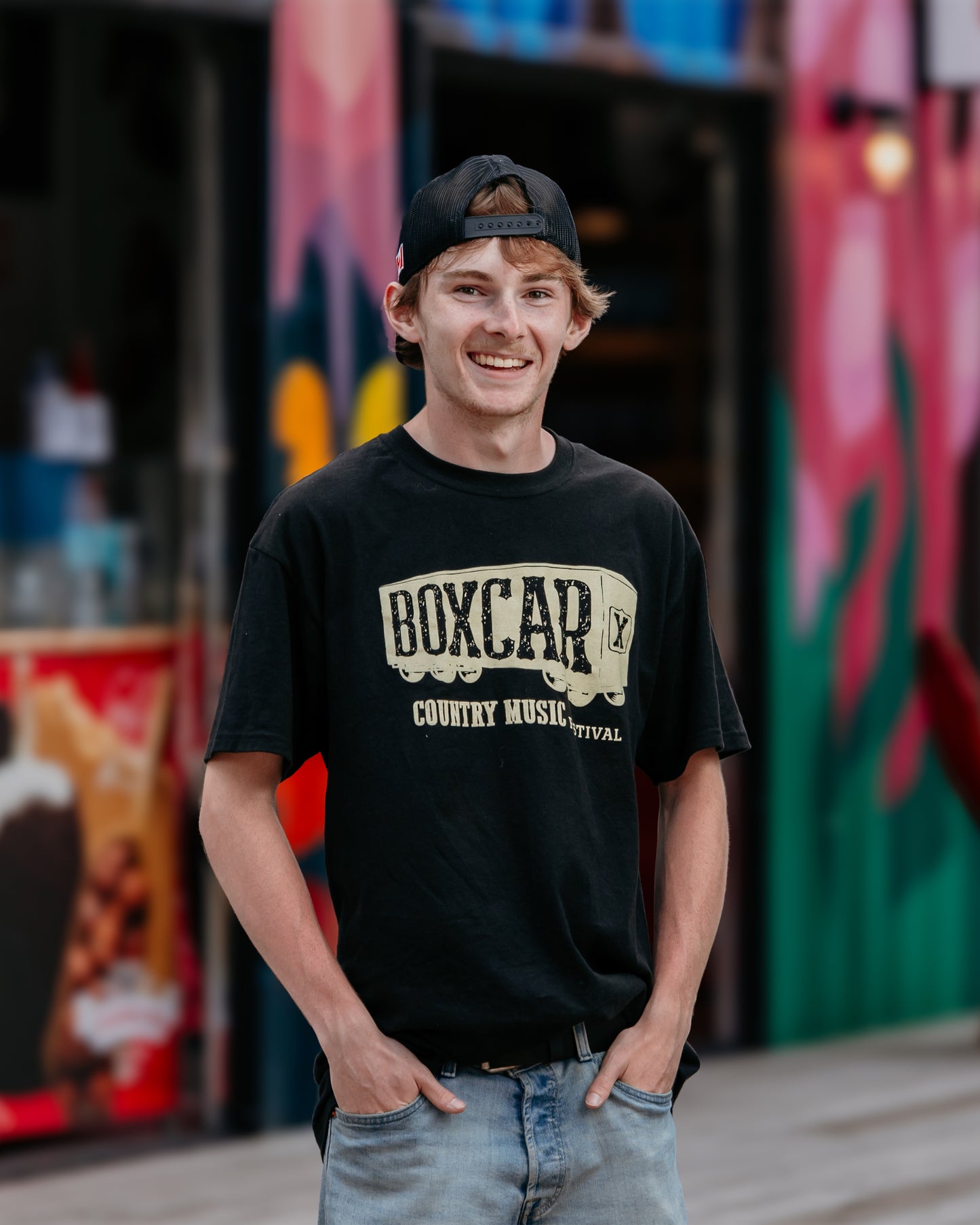A person wearing a black Boxcar Music Festival train logo t-shirt and a baseball cap.