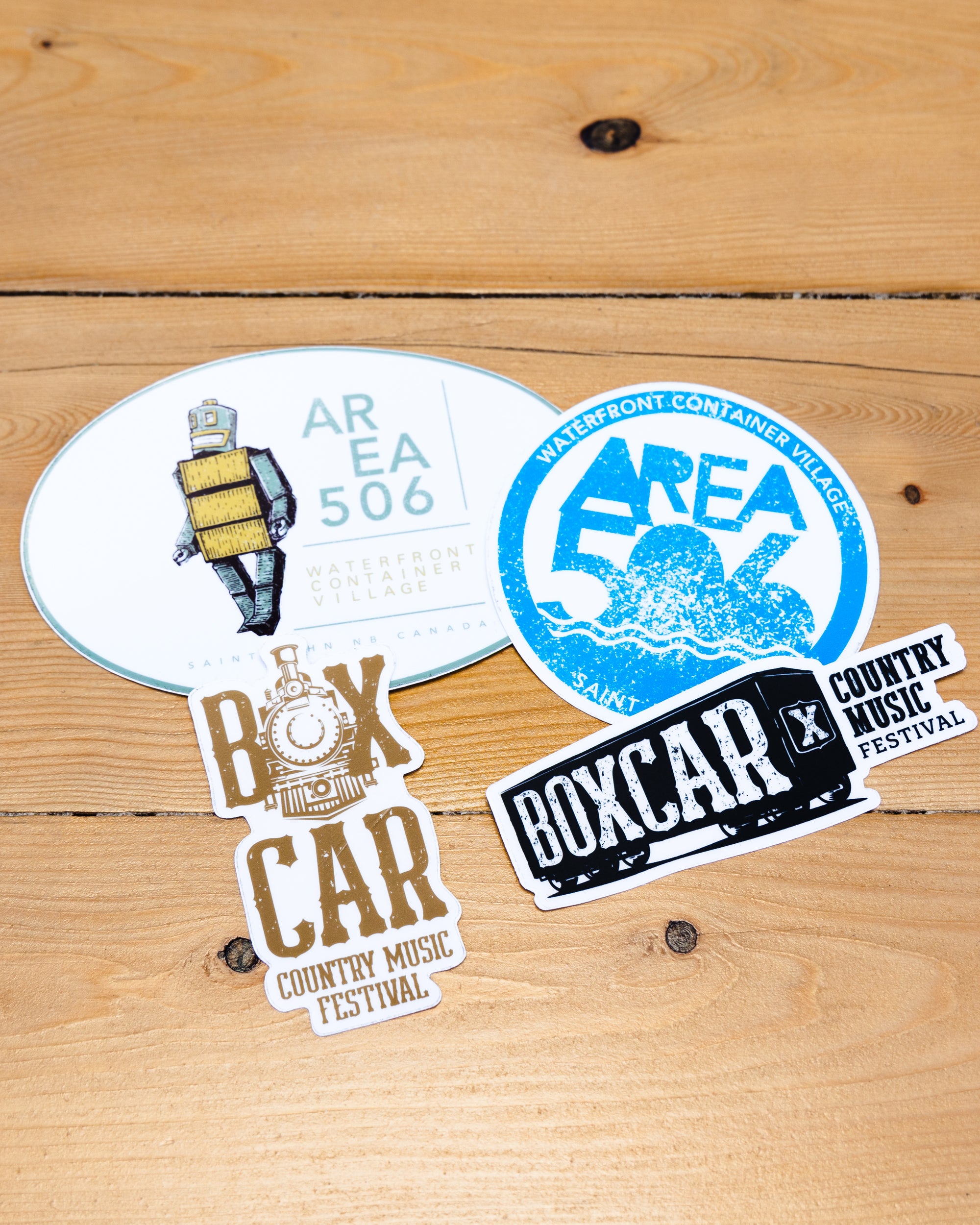 Oval AREA 506 branded with the robot mascot, blue AREA 506 Waterfront Container Village round, black Boxcar Country Music Festival, or Gold Boxcar Country Music Festival sticker.
