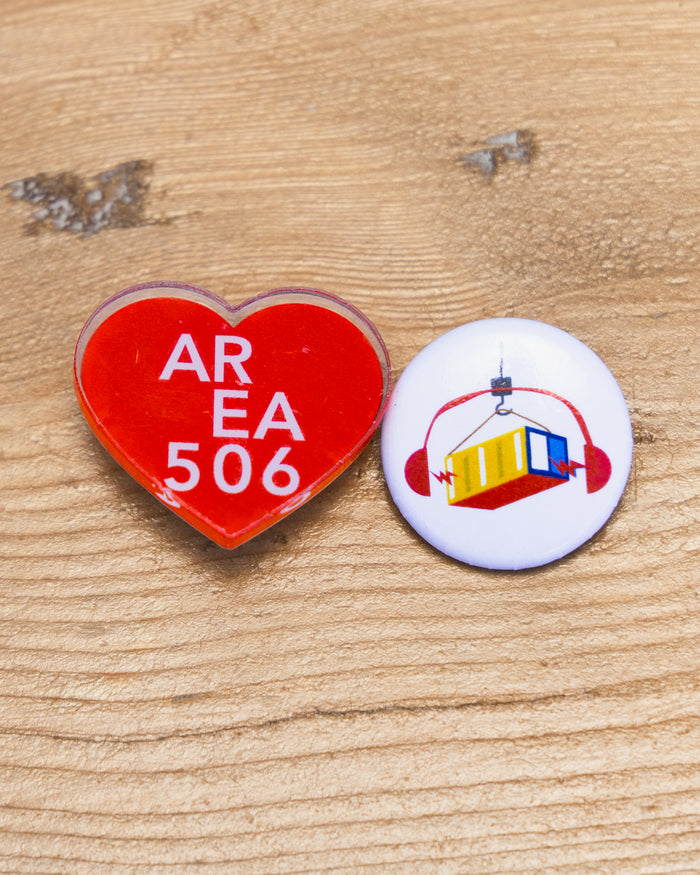 Red heart-shaped with an AREA 506 logo, or white circle-shaped with headphones and a shipping container small pin.