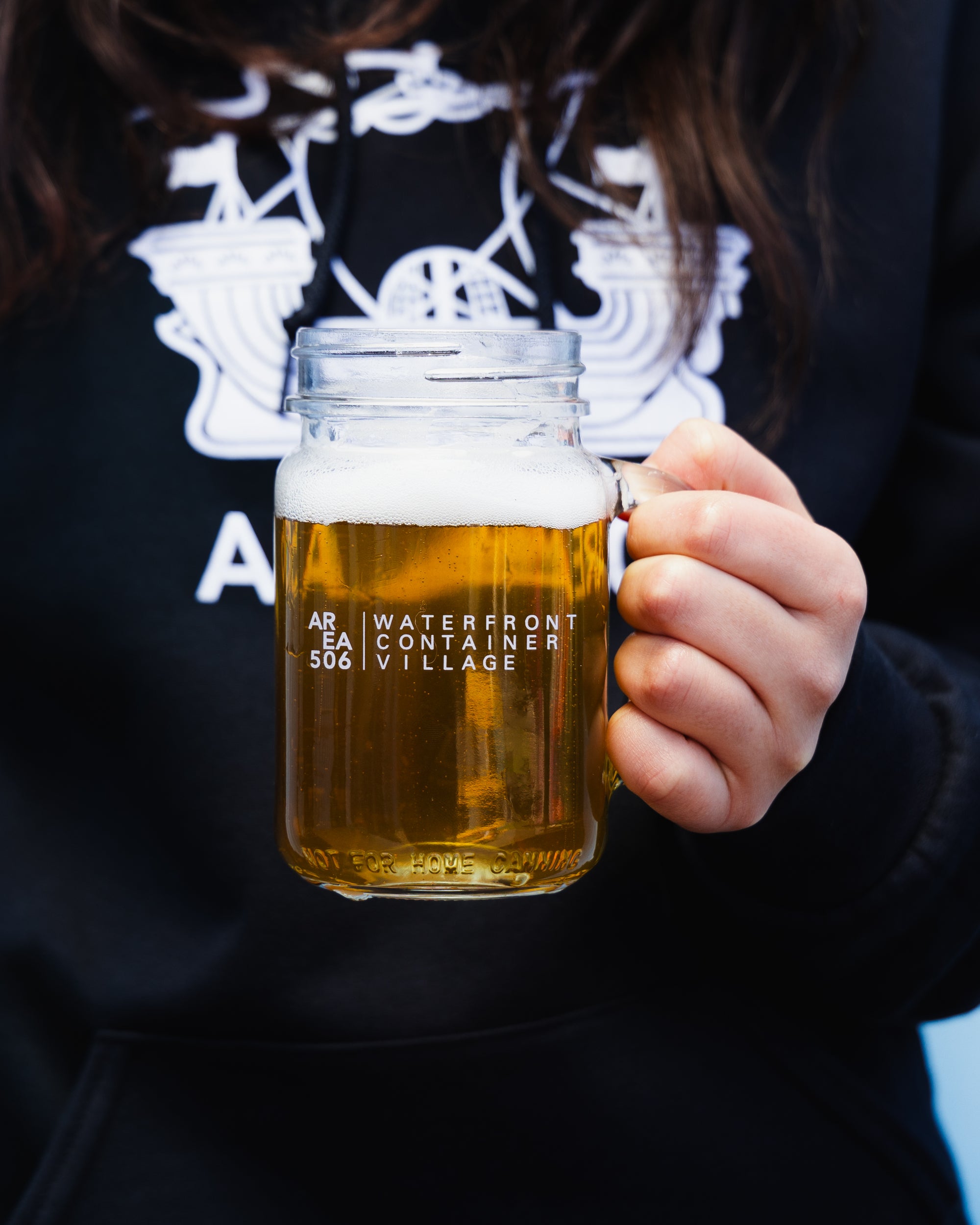 Mason jar mug with a handle for drinking, and the AREA 506 Waterfront Container Village logo.