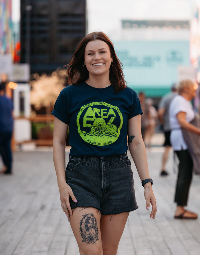 Navy blue t-shirt available in three text colours. Green, peach, or blue AREA 506 Waterfront Container Village logo on the front and left sleeve.