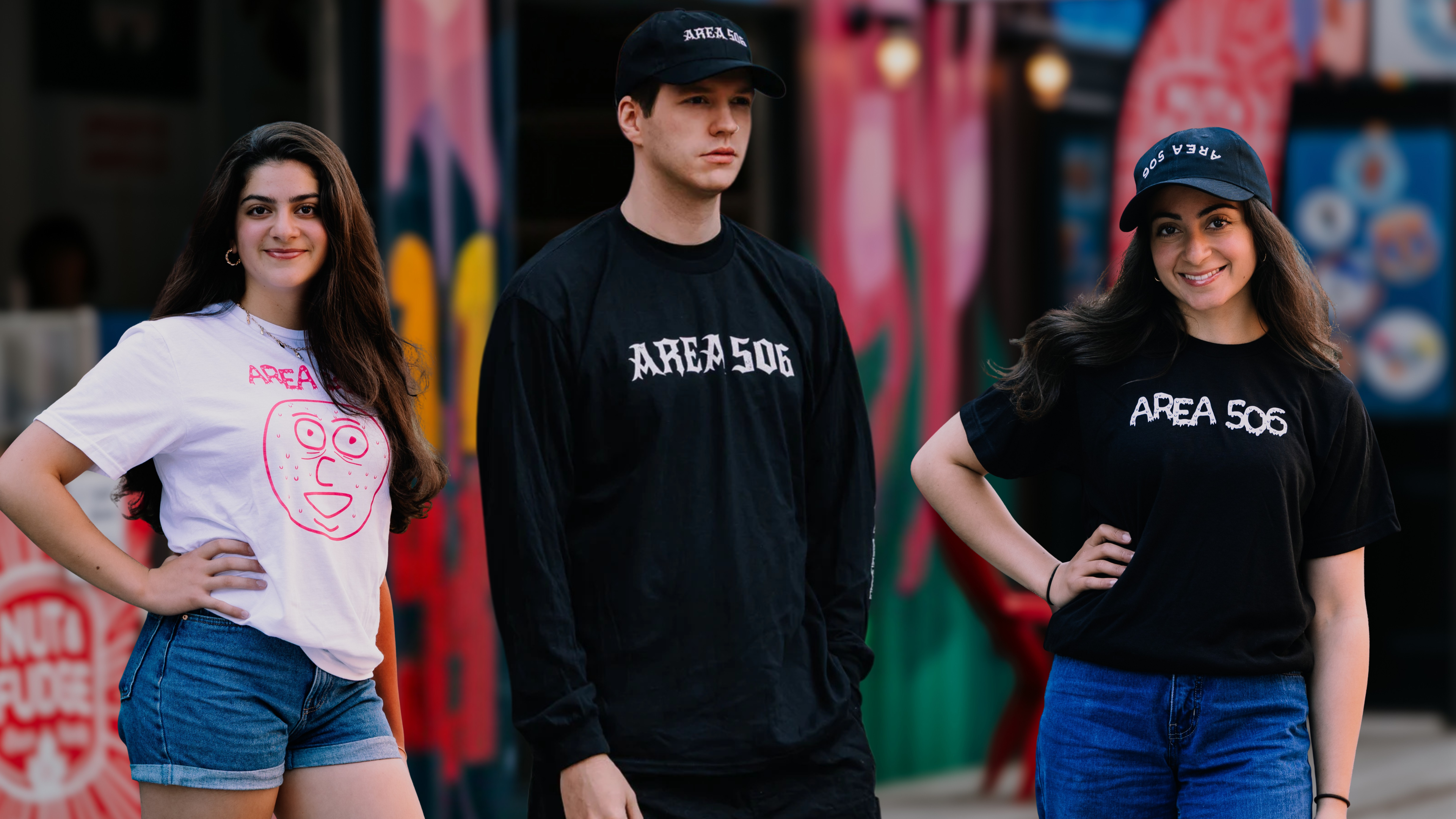 Three people wearing 'AREA 506' t-shirts in front of a colorful mural in Graffiti Alley.
