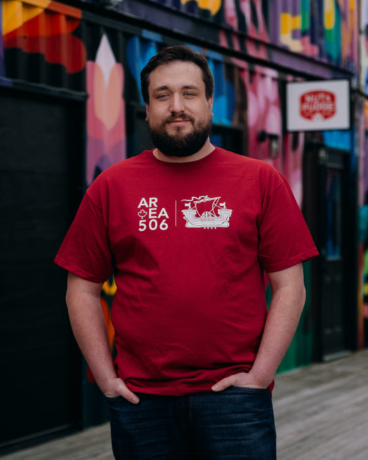 Man wearing a red t-shirt with a logo and text, standing in front of a colorful mural.