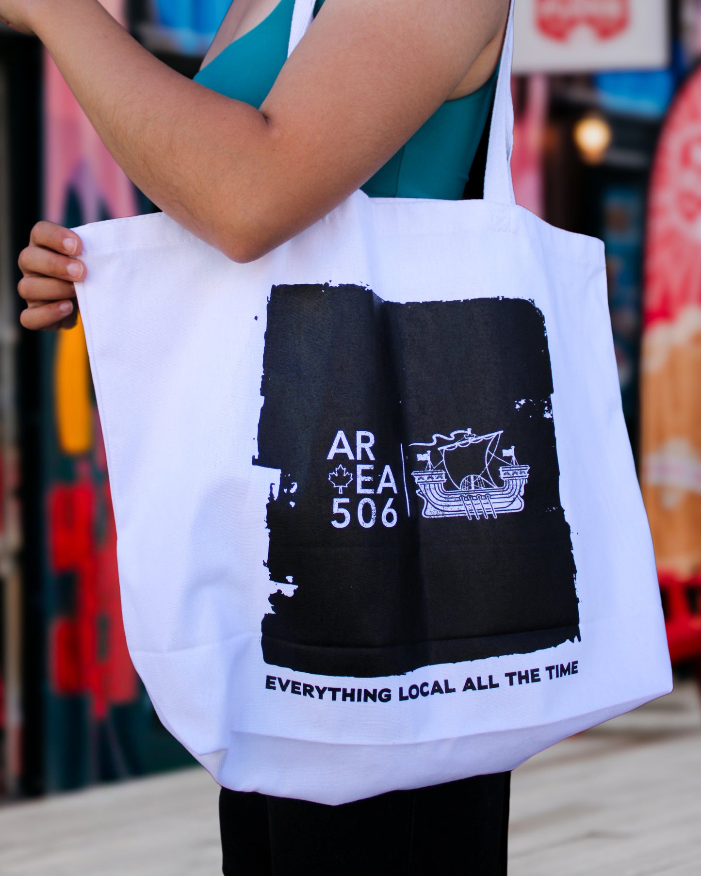 Person holding a white tote bag with black graphics and text.
