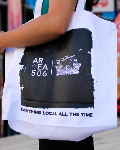 Tote bag with black and white design featuring text and a logo, held by a person.