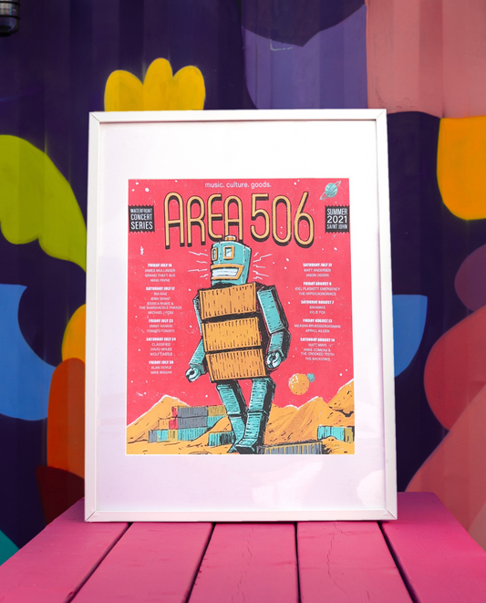 A collectible poster featuring a cartoon-style robot and the text 'AREA 506' on a vibrant red background, framed and displayed on a pink surface with a colourful background.