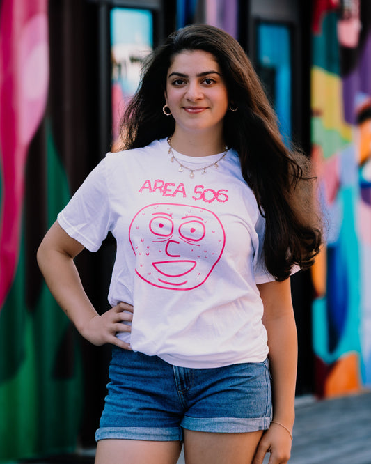 Woman wearing a white t-shirt with a pink graphic design and text, standing in front of a colorful mural.