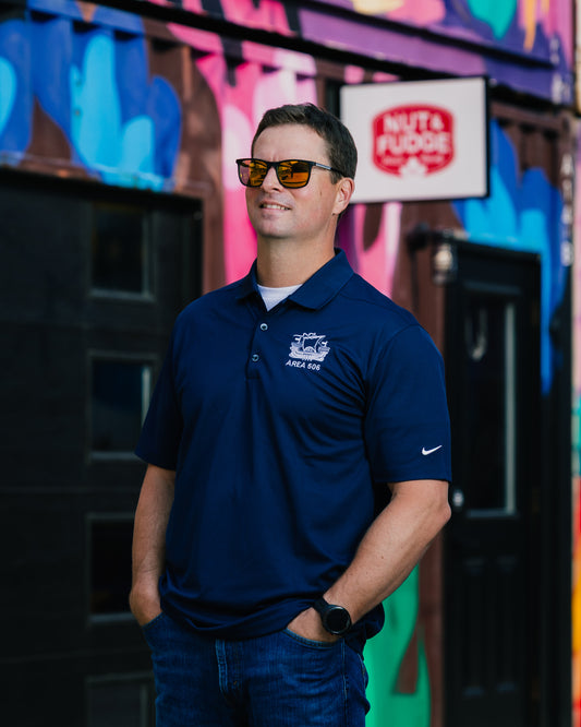 Man wearing a navy blue polo shirt with a logo in front of a colourful building.