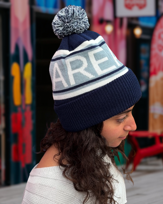 Person wearing a navy blue knit toque with a pom-pom. 'AREA 506' is knit into the fabric of the hat.