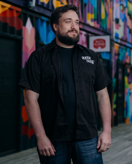 Man wearing a black shirt with a logo in front of a colourful mural.