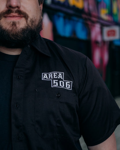 Person wearing a black shirt with 'AREA 506' logo against a colourful blurred background