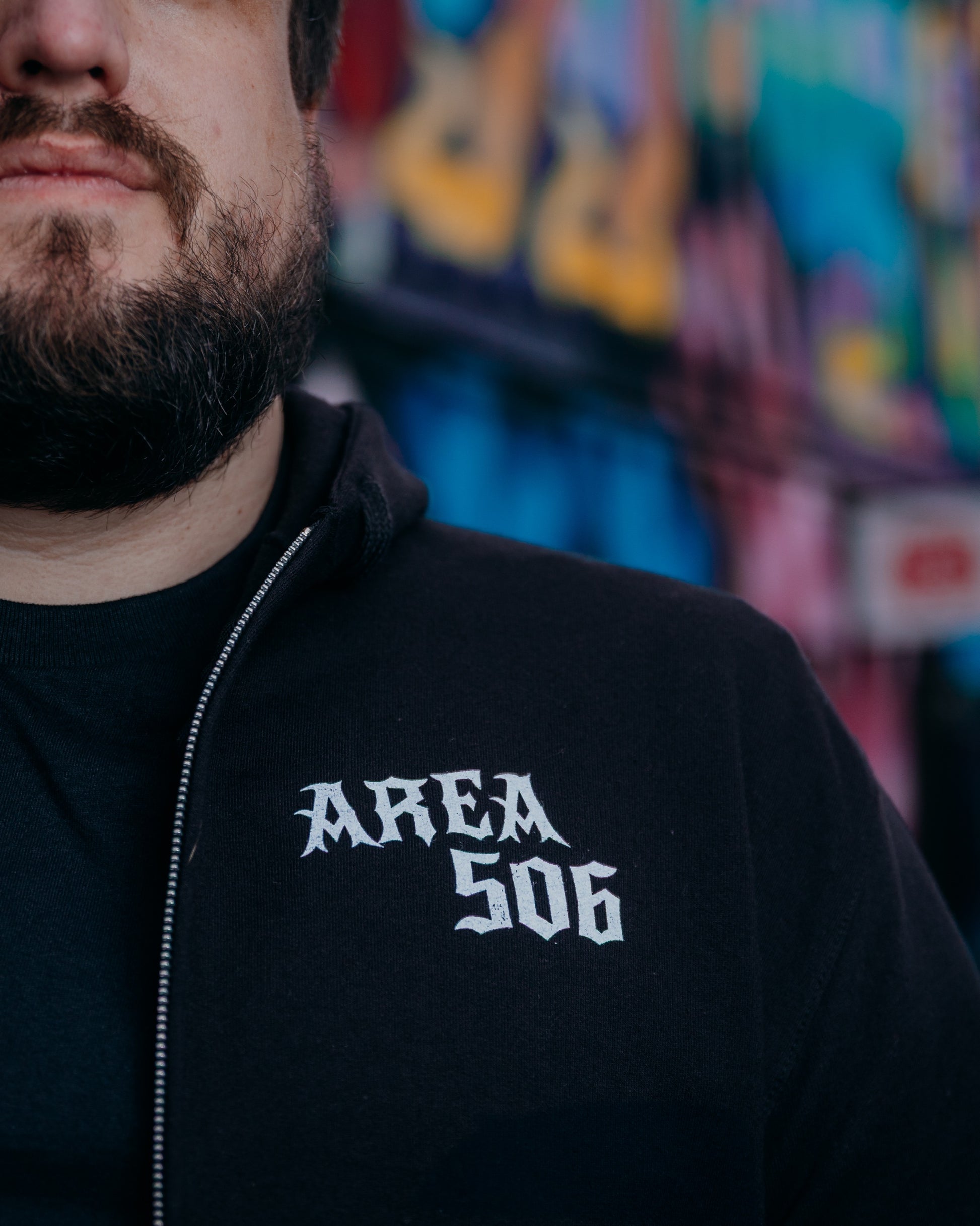 Person wearing a black hoodie with 'AREA 506' text, blurred colourful background