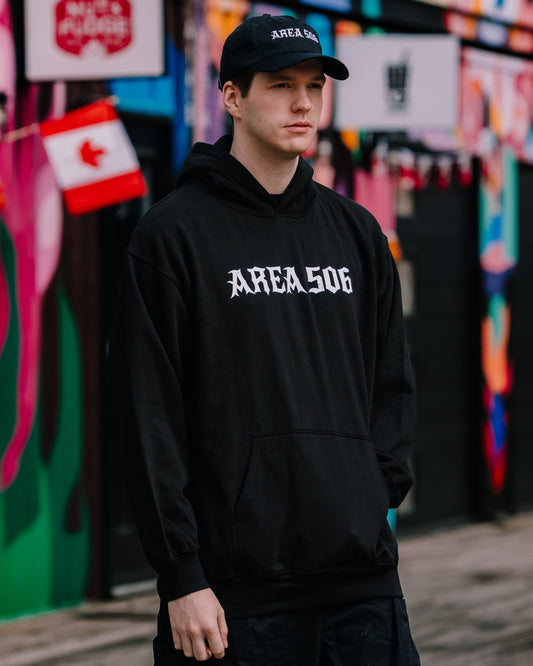 Person wearing a black hoodie with 'AREA506' white text in front of a colourful mural.