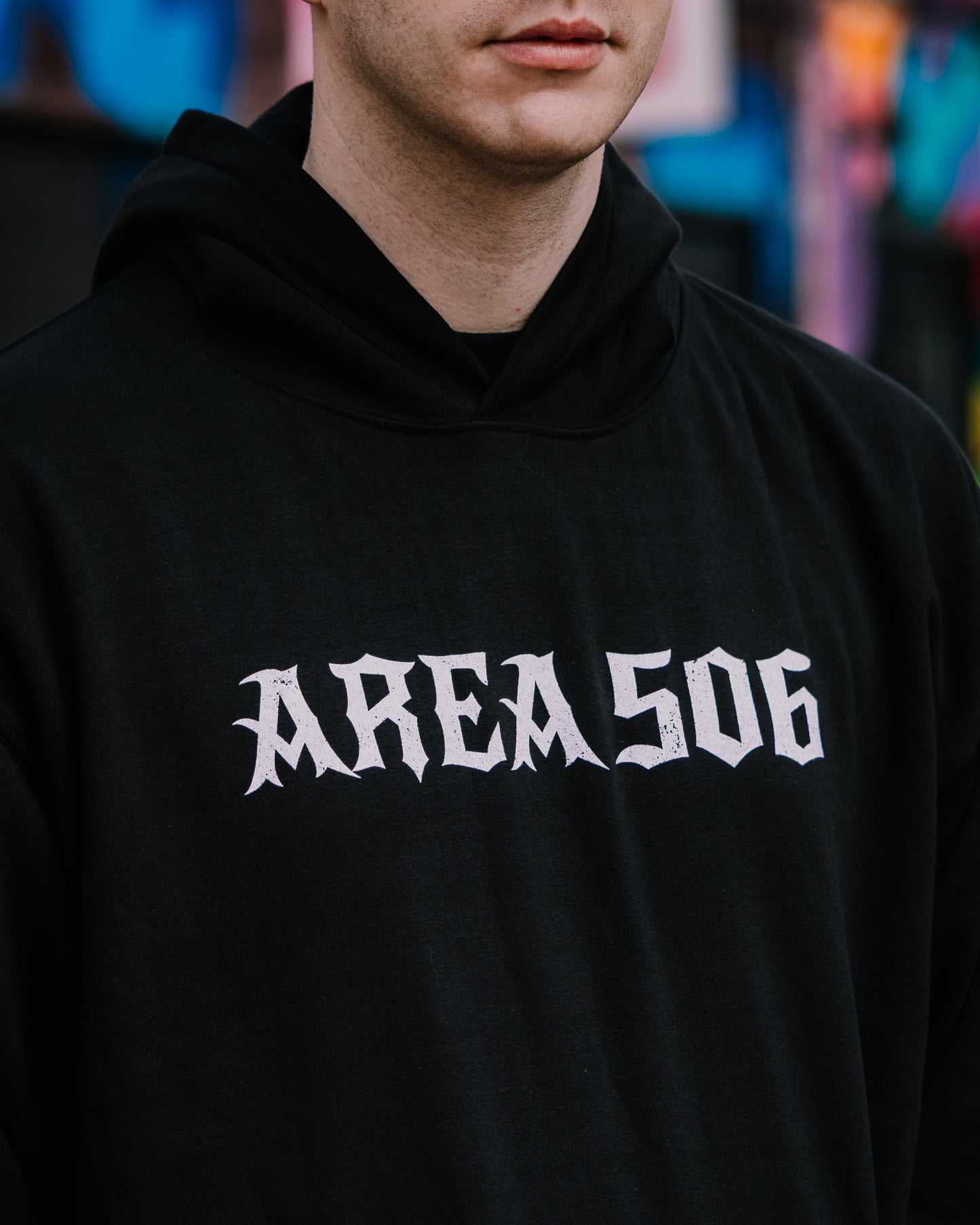 Person wearing a black hoodie with 'AREA 506' printed on it, blurred colourful background