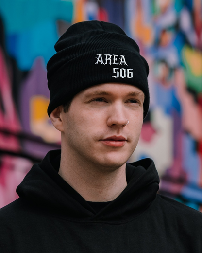 Person wearing a black beanie with 'AREA 506' text in front of a colourful graffiti wall.