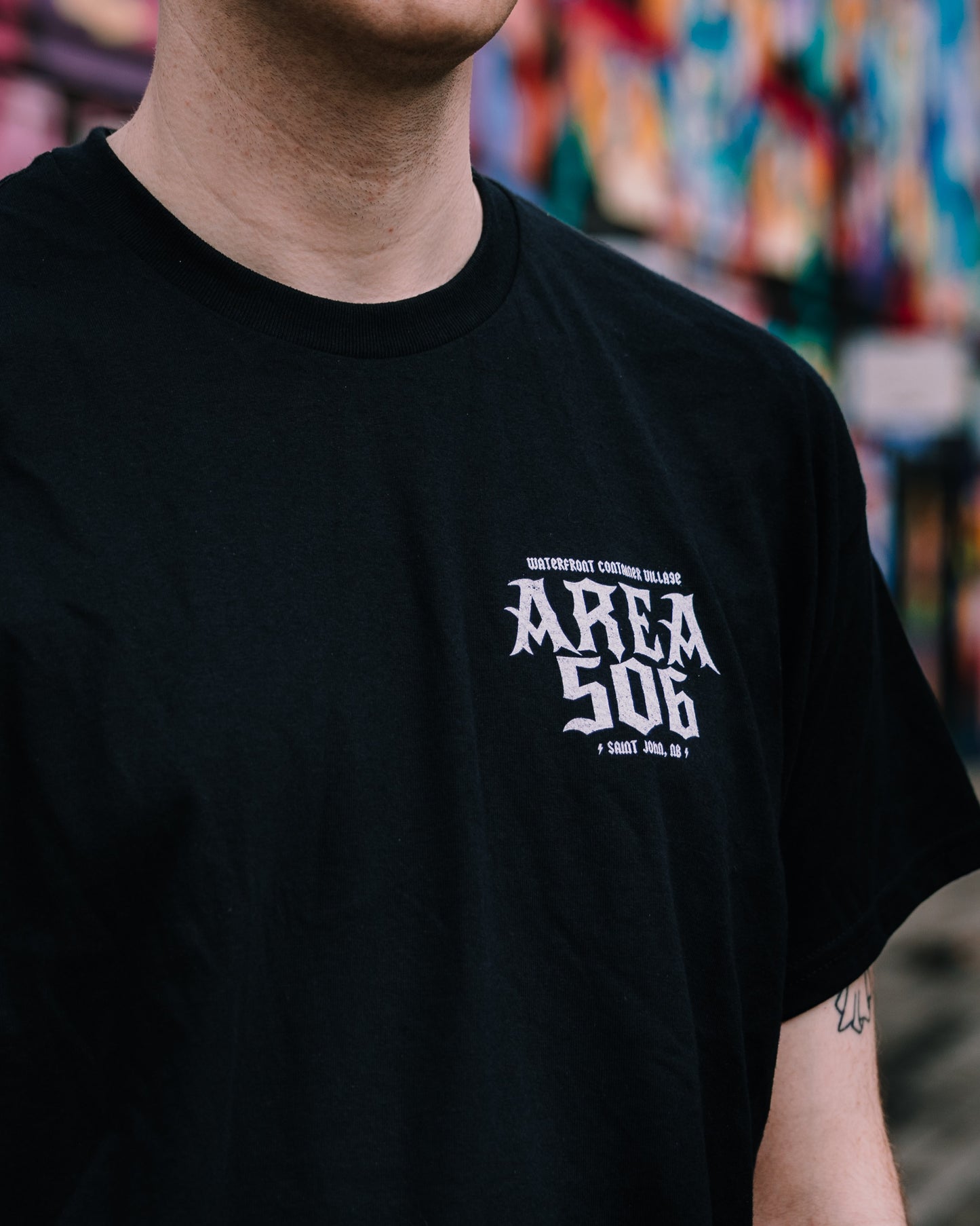 Person wearing a black t-shirt with 'AREA 506' text, blurred colourful background