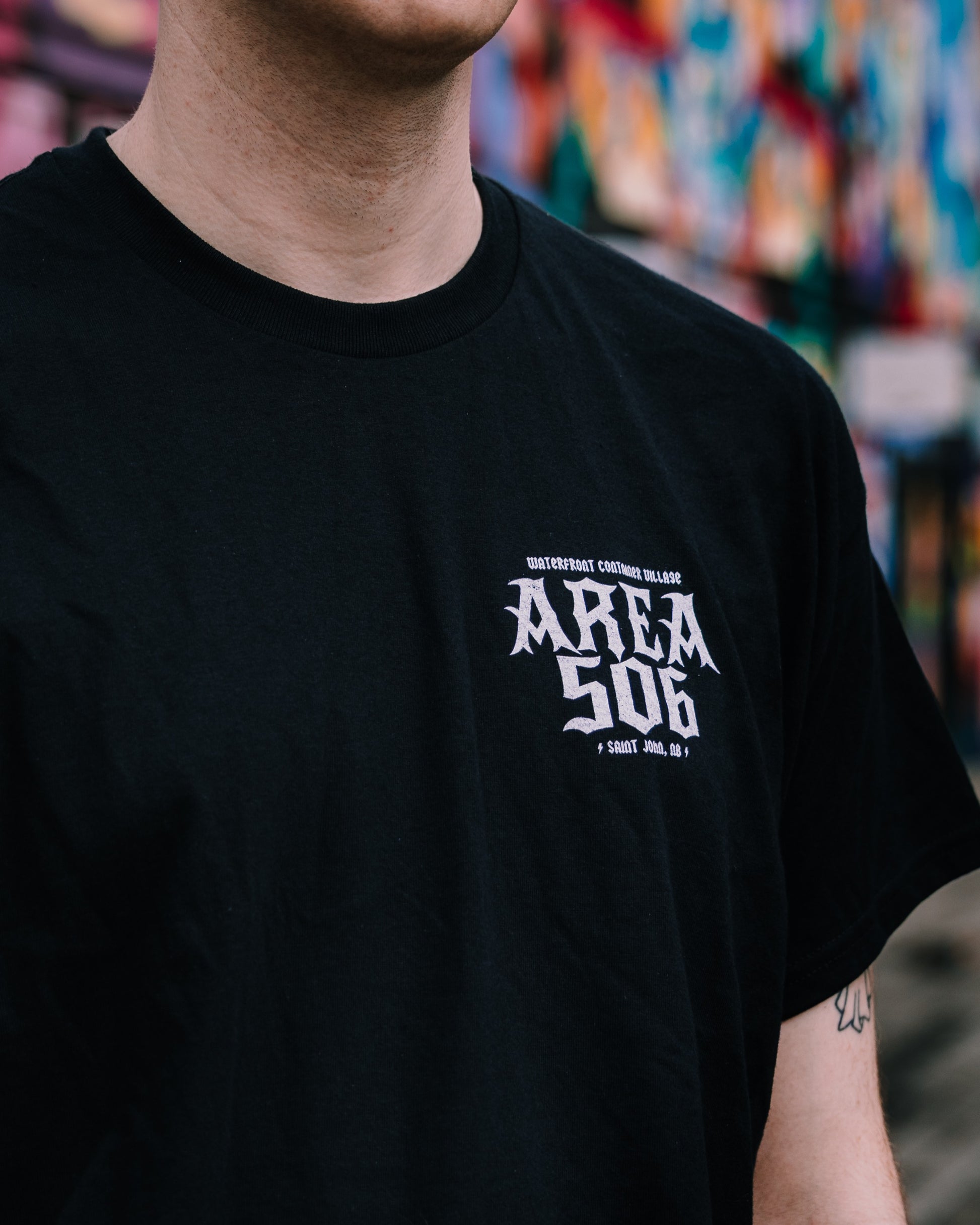 Person wearing a black t-shirt with 'AREA 506' text, blurred colourful background
