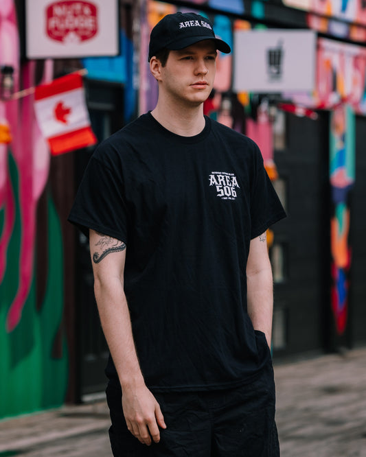 Person wearing a black t-shirt with 'AREA 506' logo in front of a colourful mural