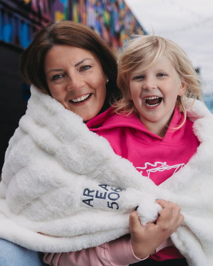 Woman and child wrapped in a white blanket with 'Area 506' text, smiling outdoors.