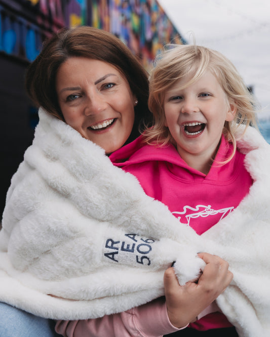Woman and child wrapped in a white blanket with 'Area 506' text, smiling outdoors.