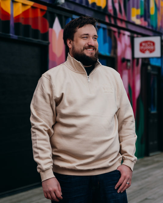 Man wearing a beige pullover standing in front of a colourful mural.