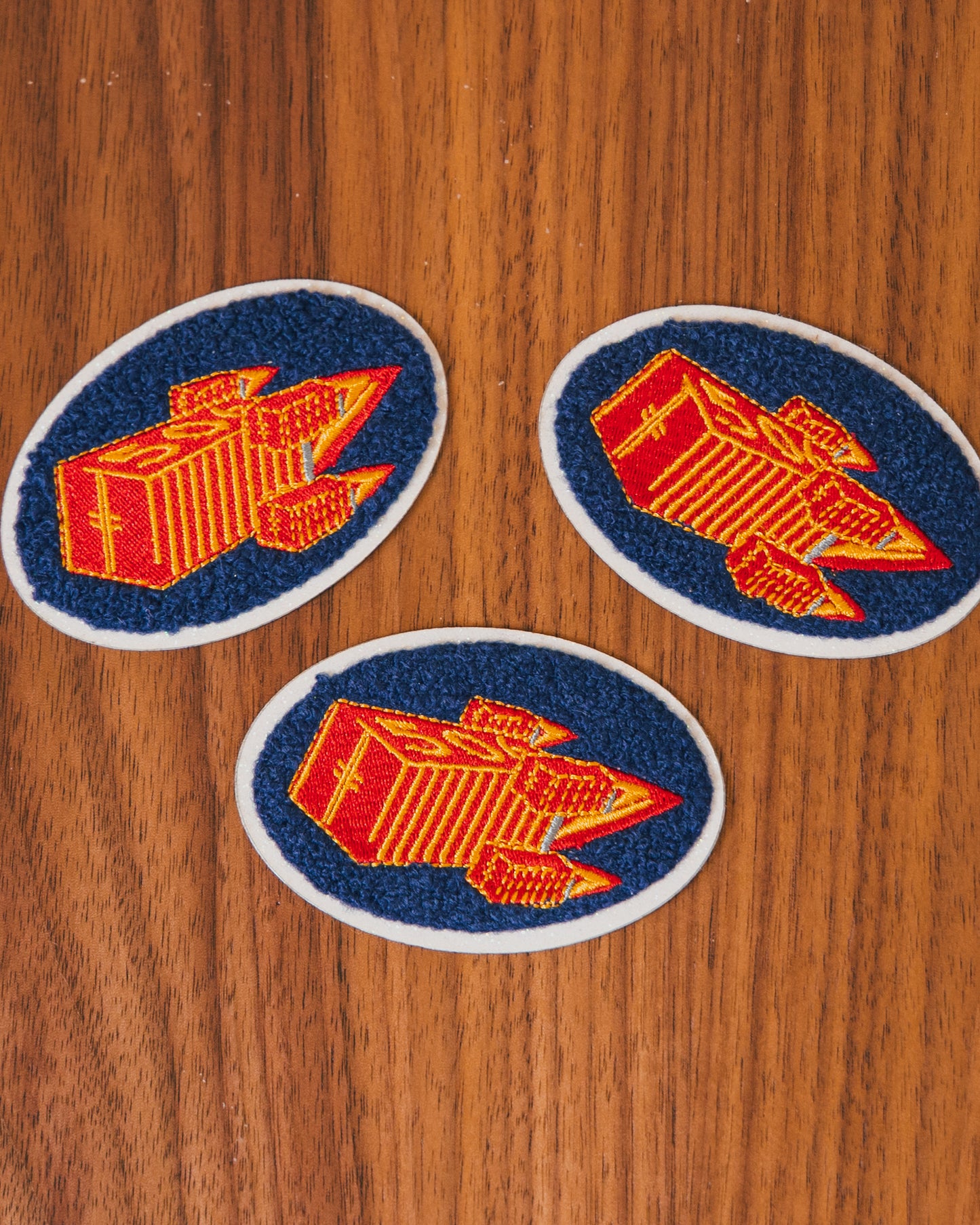 Three embroidered patches of an orange, red, and blue design on a wooden surface