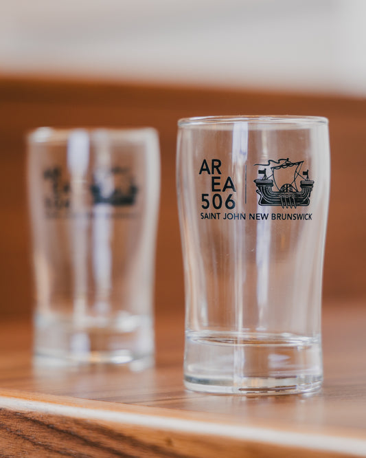 Two shot glasses with 'AREA 506 Saint John New Brunswick' text and logo on a wooden surface.