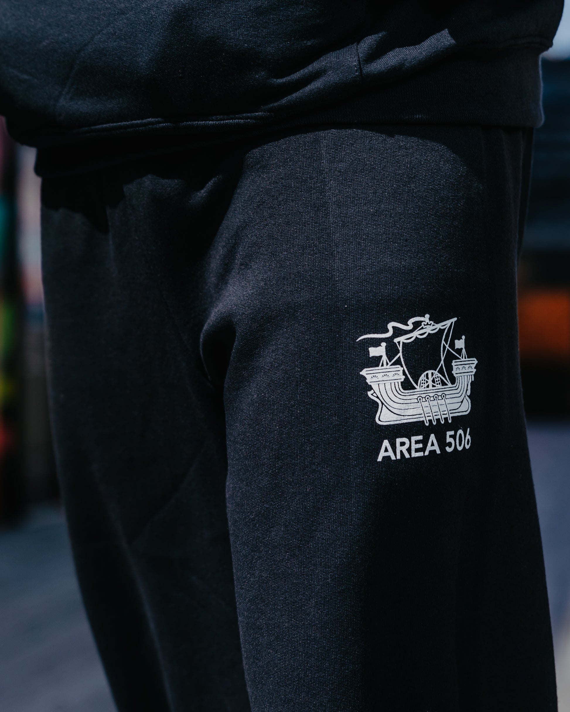 Black sweatpants with the AREA 506 galley ship logo printed on the top left leg.