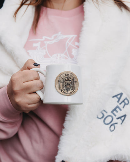 Person holding a white mug with a logo, wearing a pink shirt and white blanket.