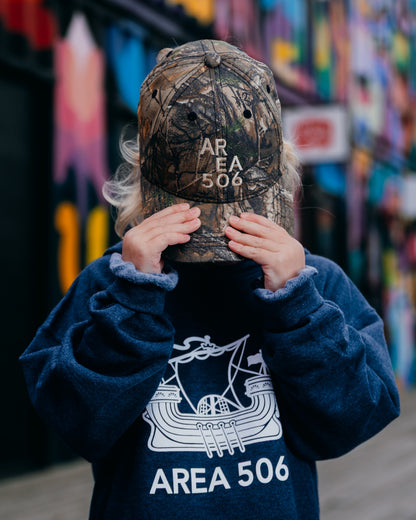 Child wearing a cap with 'AREA 506' text, in front of a colourful mural.