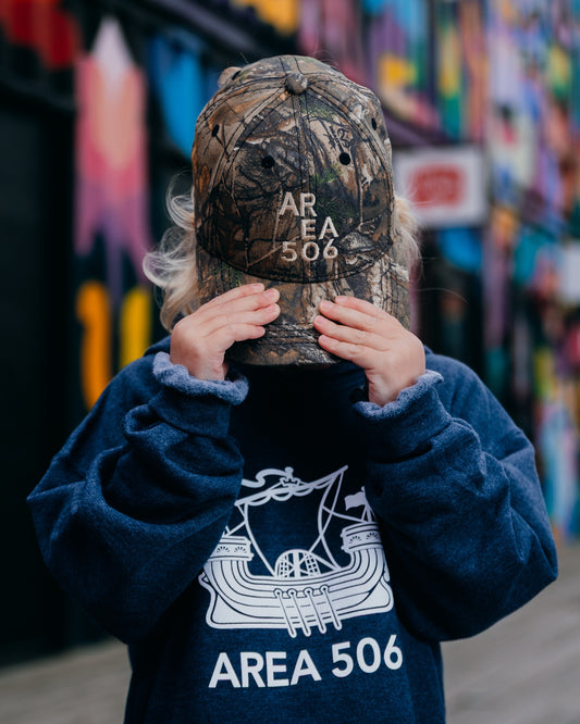 Child wearing a cap with 'AREA 506' text, in front of a colourful mural.