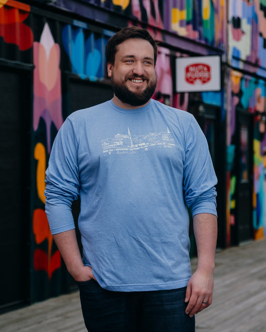 Man wearing a blue shirt with white line drawing, standing in front of a colourful mural.