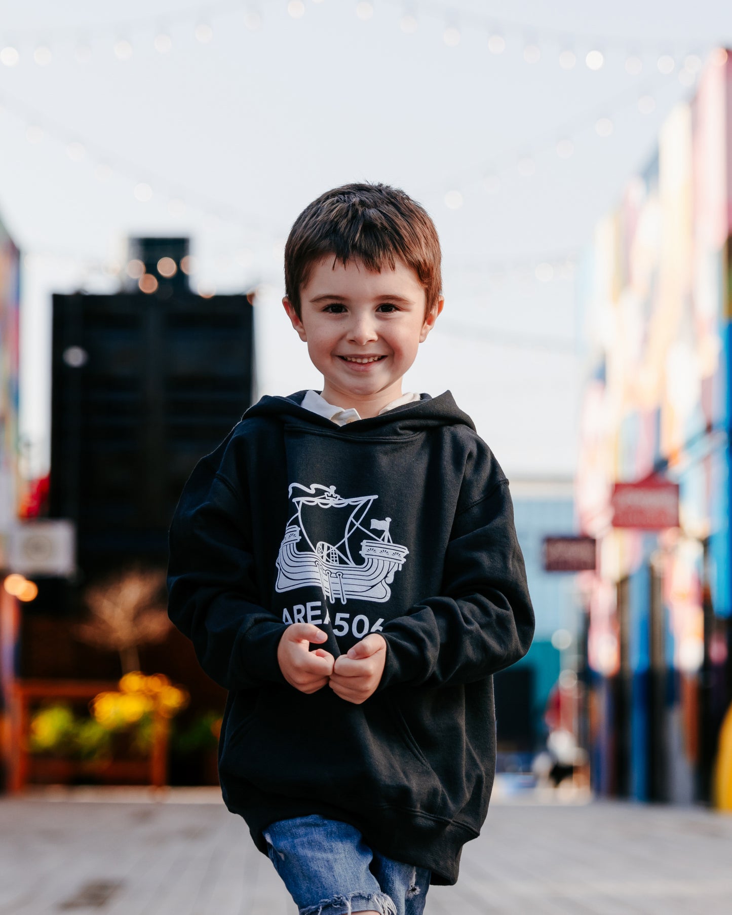 Child wearing a black hoodie with 'AREA 506' design in front of a colourful mural.