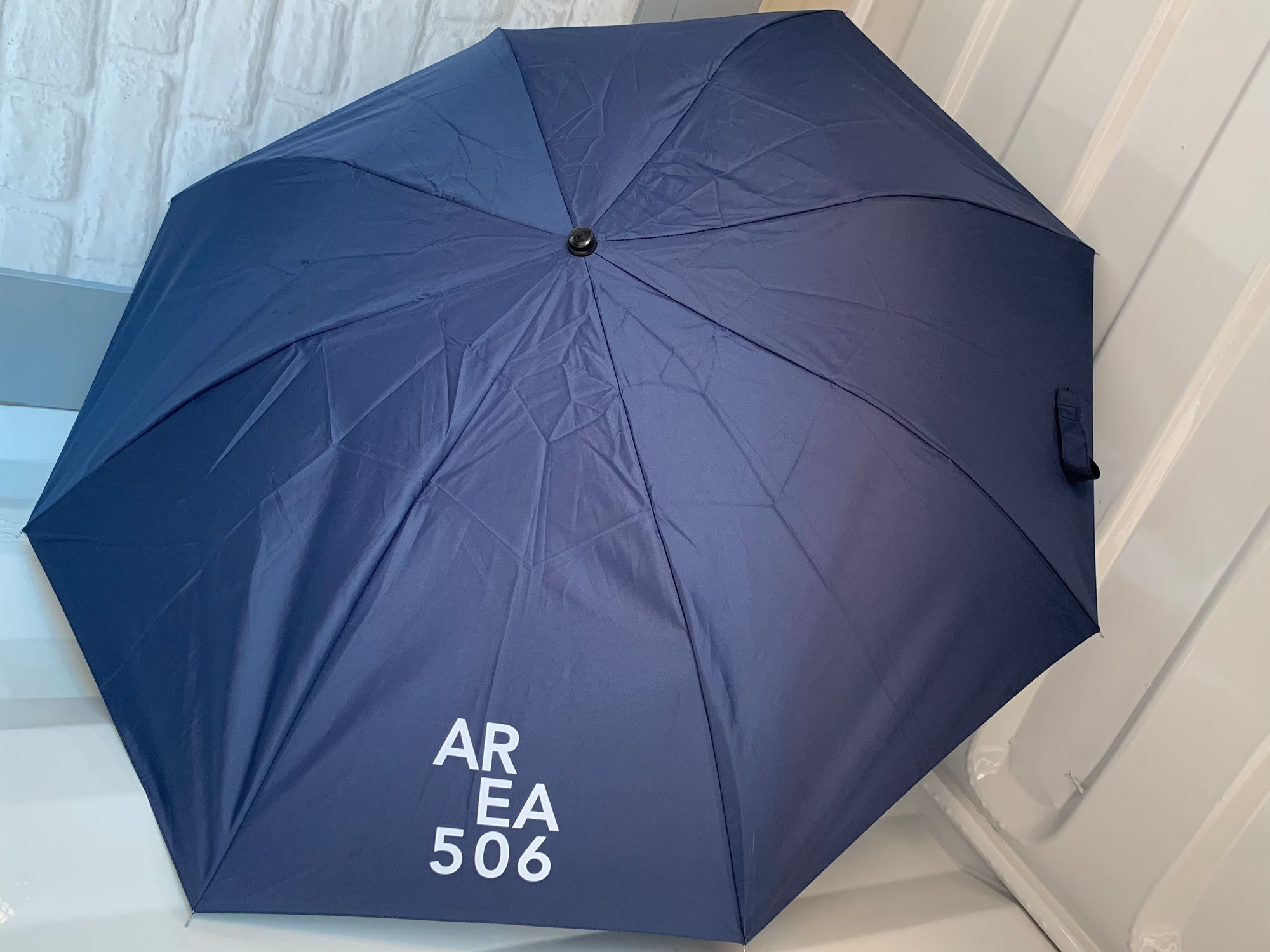 Navy blue umbrella with a white AREA 506 logo screened on one panel.